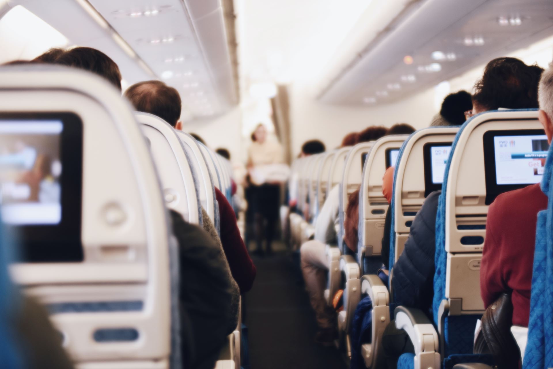 An airplane with seated passanger watching screens and staff delivering drinks