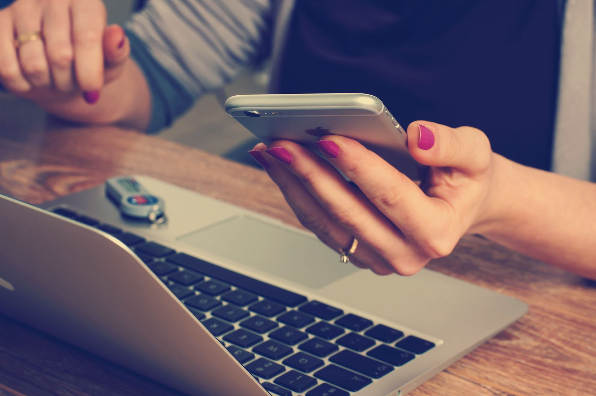 A person sitting at a desk with a laptop and a mobile phone in the left hand