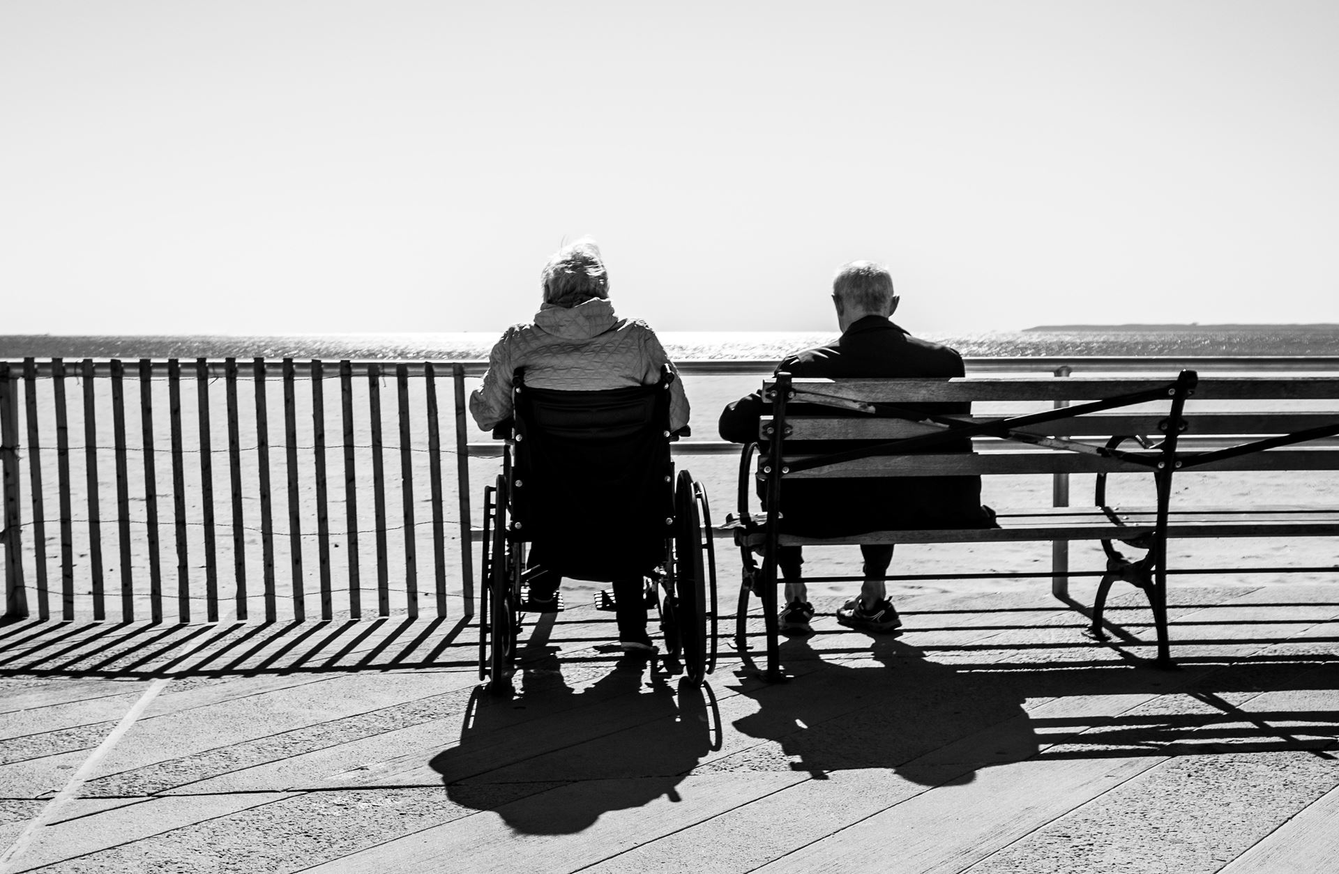 two people sitting on a bench and in a wheelchair next to the bench