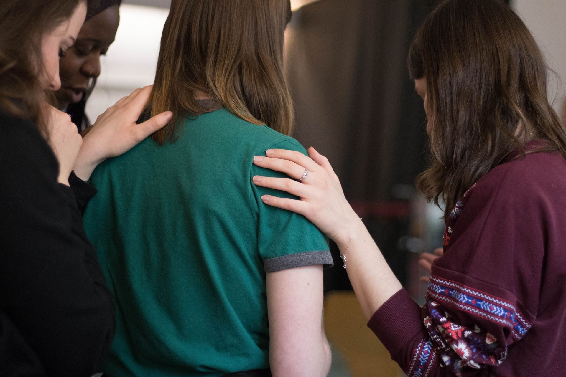 a group of people with their hands on a persons shoulders, offering comfort