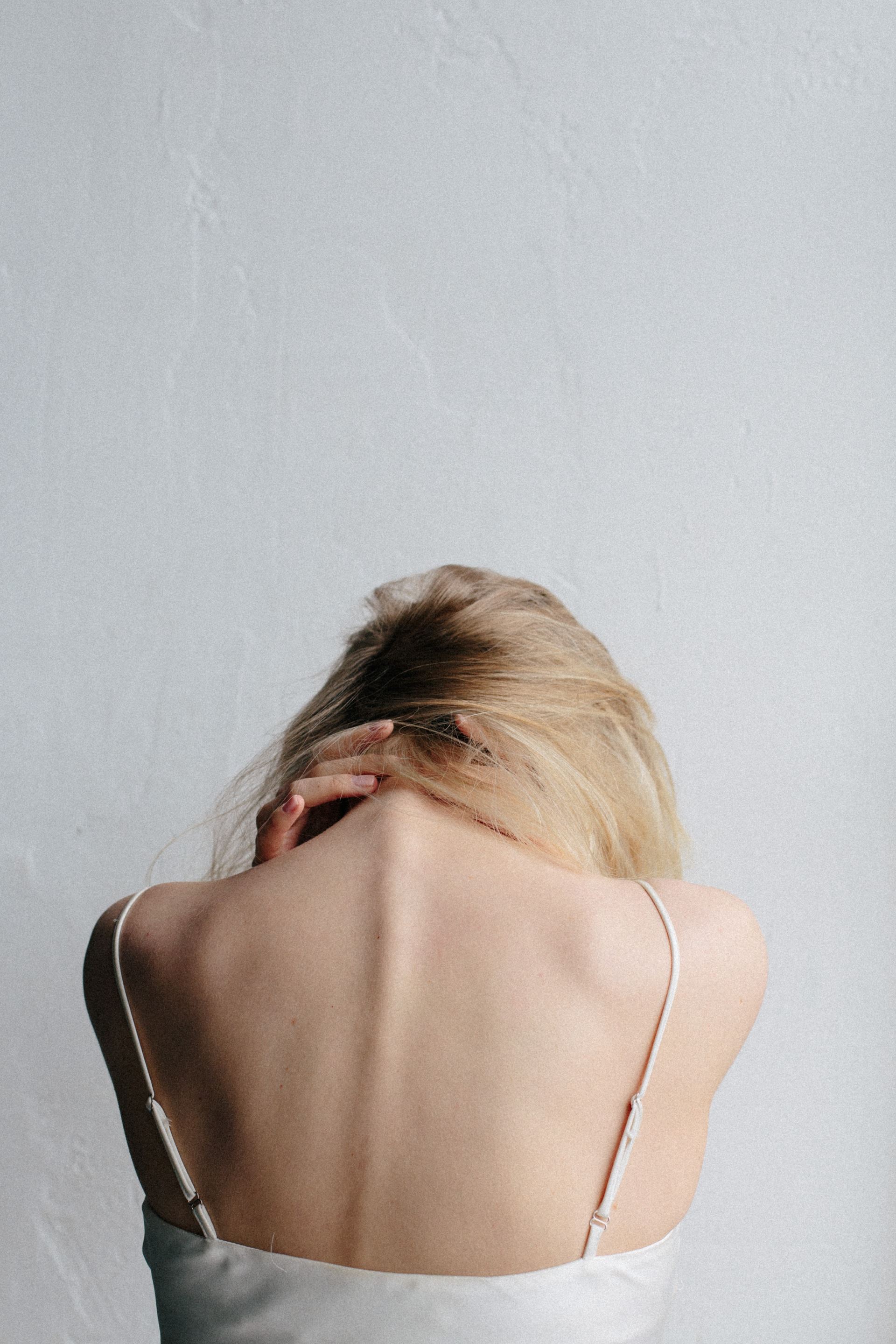 A woman with blonde hair rubbing the back of her neck in pain