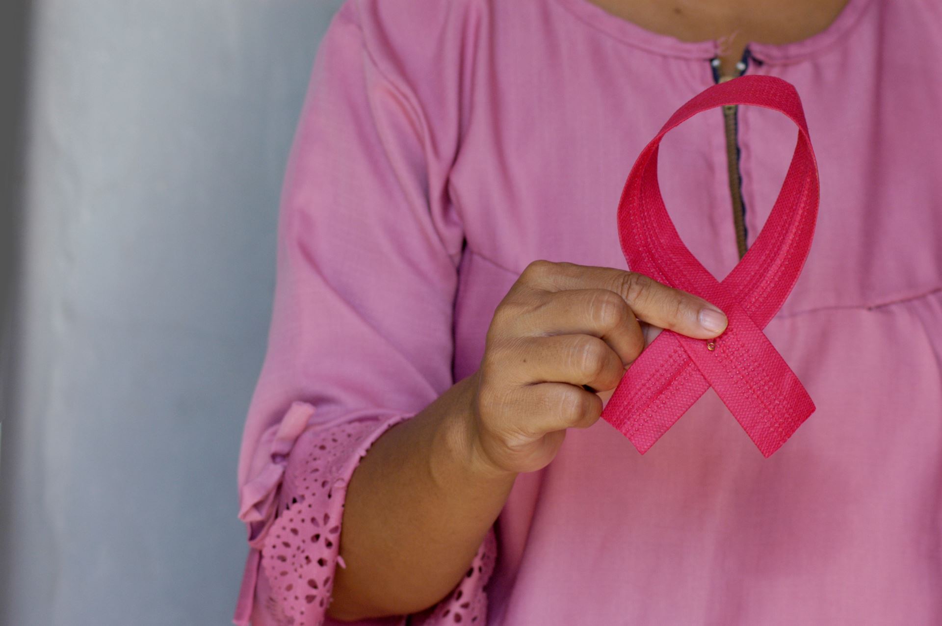 As person in a pink shirt holding a pink ribbon for breast cancer awareness