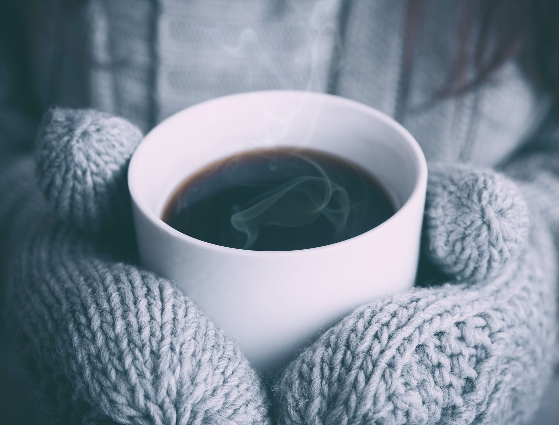 a person wearing wooly gloves holding a hot cup of coffee