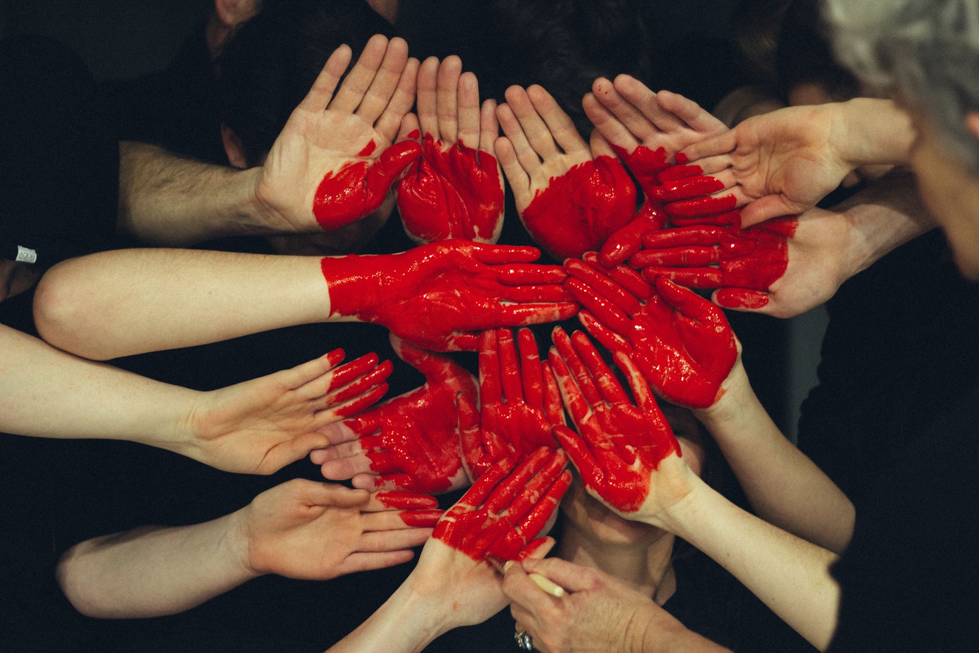 A group of hands with red pain o, grouped together to create a heart image